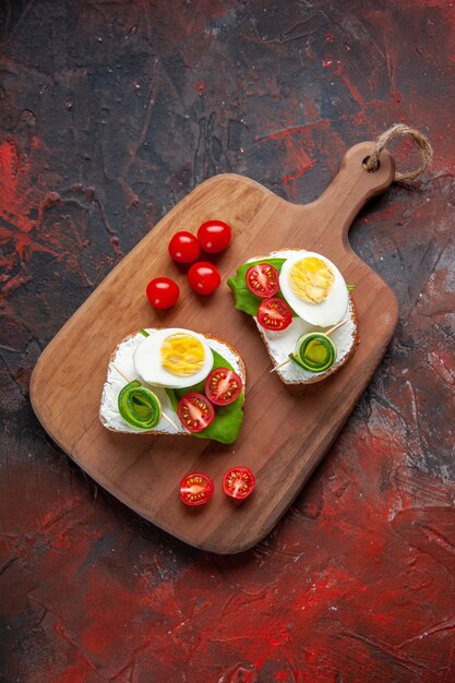 Vista superior sabrosos sándwiches de huevo con tomates rojos en tabla de cortar fondo rojo oscuro almuerzo tostadas bocadillo comida pan comida hamburguesa