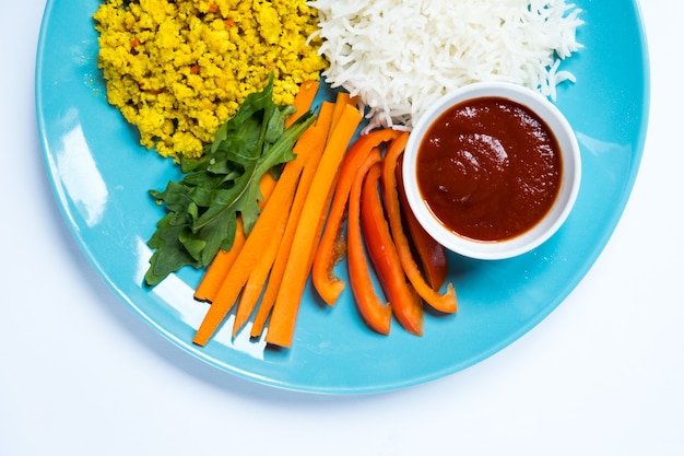 Vista superior de la salsa de tomate de alimentos dietéticos y verduras con un tenedor junto a una placa azul sobre un fondo blanco.