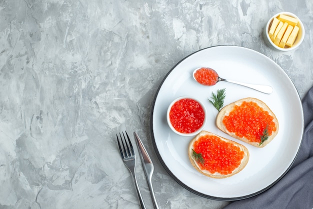 Vista superior sándwiches de caviar placa interior con cubiertos sobre superficie blanca