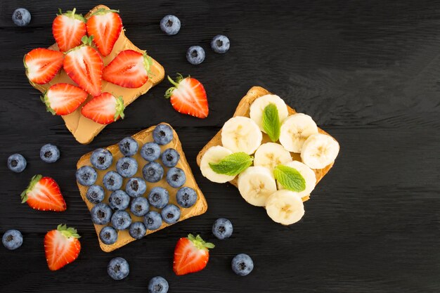 Vista superior de sándwiches con mantequilla de maní y frutas en el negro