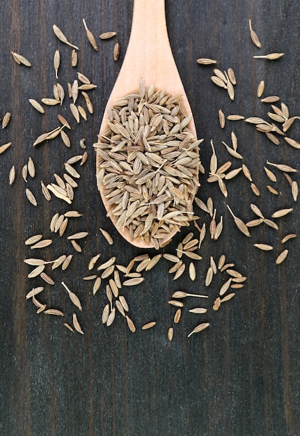 Vista superior de semillas de comino secas en una cuchara de madera con algunas esparcidas sobre la mesa