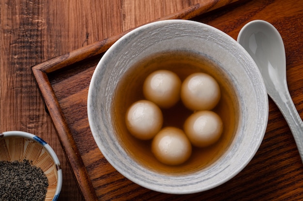 Vista superior de sésamo grande tangyuan (tang yuan, bolas de bola de masa de arroz glutinoso) con sopa de jarabe dulce en un recipiente sobre fondo de mesa de madera para la comida del festival del solsticio de invierno.