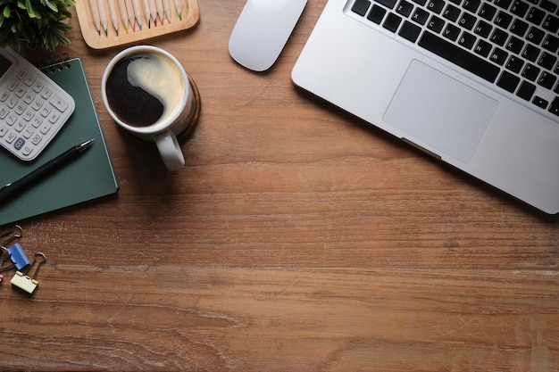 Vista superior simples local de trabalho com calculadora de xícara de café de computador portátil e planta em vaso sobre fundo de madeira