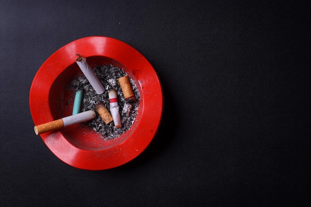 Vista superior de las sobras de cigarrillos y las colillas de cigarrillo en círculo rojo desviado sobre fondo negro con co
