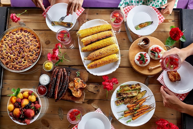 Foto vista superior sobre una mesa de comedor, decorada con flores, con vajilla y comida. picnic en el patio trasero con amigos o vecinos, cena familiar.