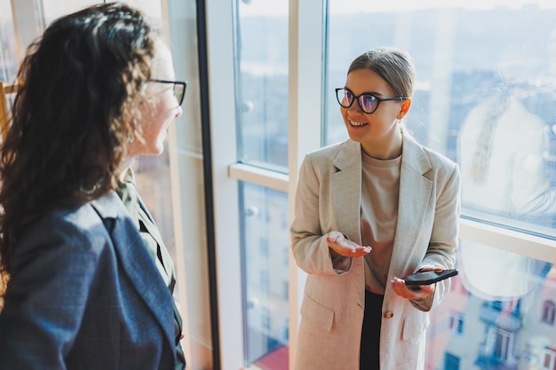 Vista superior de sonrientes jóvenes trabajadores de negocios confiados en ropa casual de pie en el fondo de la oficina moderna y hablando durante el descanso del día