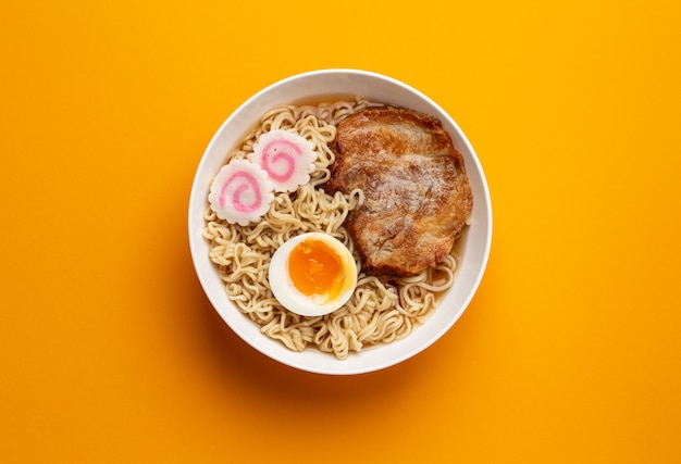 Vista superior de la sopa de fideos japoneses ramen en un tazón blanco con fideos, caldo de carne, cerdo asado en rodajas, narutomaki, huevo con yema sobre fondo naranja brillante. Plato tradicional de Japón, primer plano