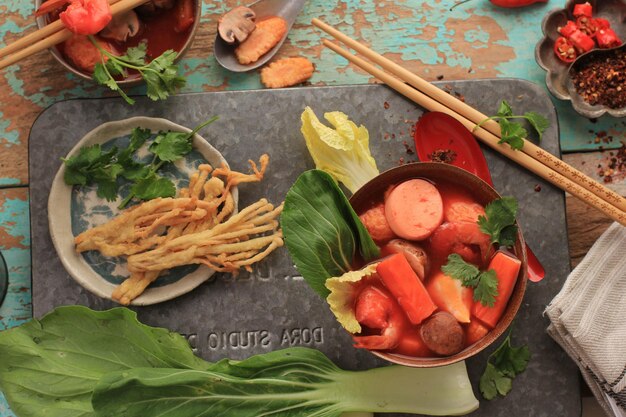 Vista superior Sopa tailandesa picante de Tom Yum con mariscos, servida en un tazón marrón rústico, sobre fondo de madera verde