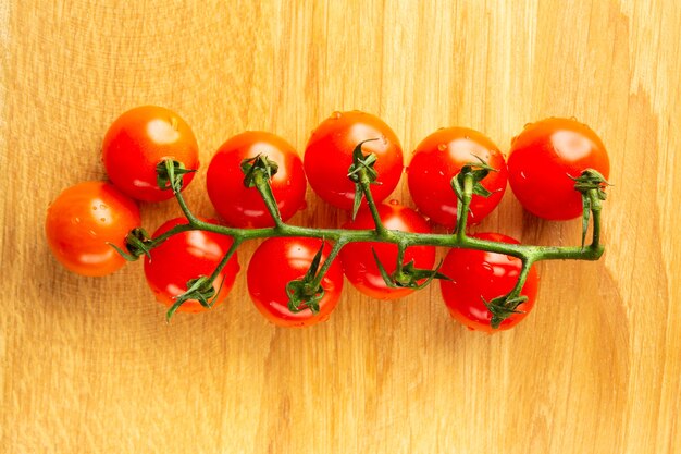 Vista superior de la superficie de madera y una rama limpia y húmeda de tomates cherry colocados sobre ella