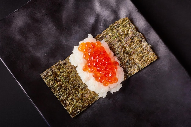 Vista superior del sushi de huevas de salmón Ikura Sushi sobre algas secas colocadas en un plato negro aislado sobre fondo negro comida japonesa popular