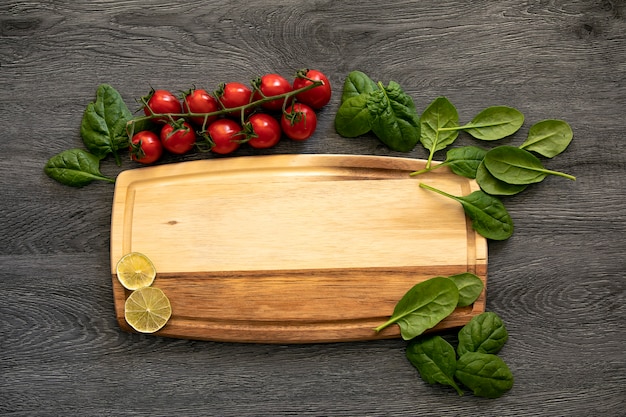 Foto vista superior de una tabla de comida de madera con espacio de copia para texto, ramas de tomates, rodajas secas de limas y hojas de espinaca