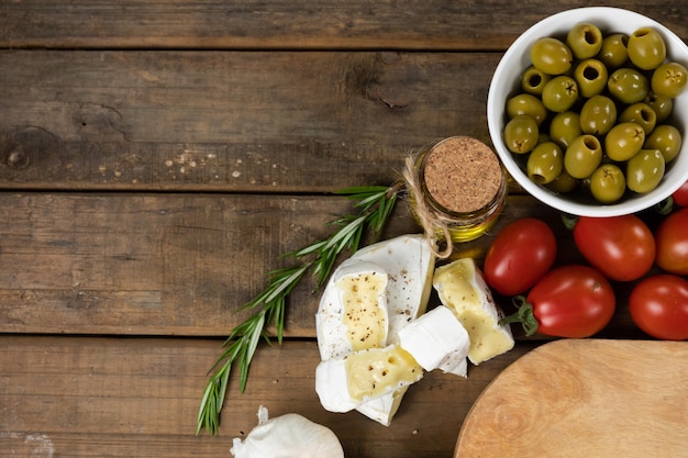 Vista superior de una tabla de cortar de madera con un plato de aceitunas verdes, un poco de queso, tomates cherry y un manantial de tomillo fresco, dispuestos sobre una superficie de madera texturizada.