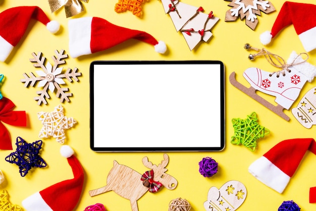 Foto vista superior de la tableta digital con decoraciones navideñas y sombreros de papá noel sobre fondo amarillo concepto de vacaciones felices