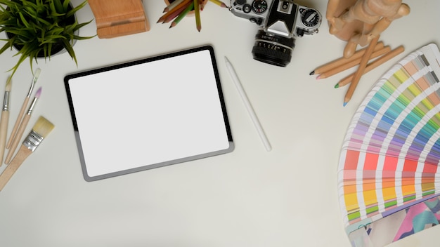 Vista superior de la tableta con trazado de recorte en la mesa de trabajo con herramientas de pintura, cámara, material de oficina y espacio de copia