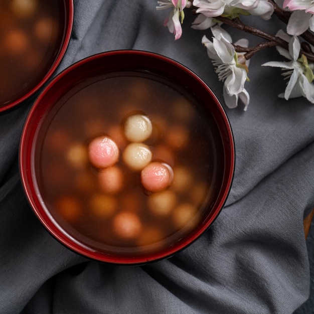 Vista superior de tangyuan rojo y blanco (tang yuan, bolas de bola de masa de arroz glutinoso) con sopa de jarabe dulce en un recipiente sobre fondo azul para la comida del festival del solsticio de invierno.