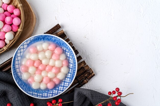 Vista superior de tangyuan rojo y blanco (tang yuan, bolas de bola de masa de arroz glutinoso) en un tazón azul sobre fondo blanco para la comida del festival del solsticio de invierno.