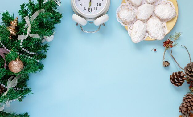 Vista superior de la tarjeta de felicitación de Navidad de maqueta y árbol de año nuevo, flatlay sobre un fondo azul con conos de abeto, reloj, galletas, lugar para su texto en una hoja blanca en el medio.