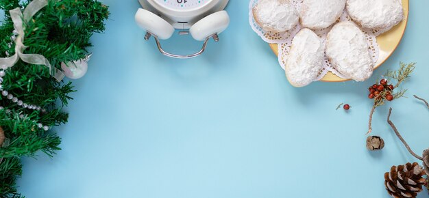 Vista superior de la tarjeta de felicitación de Navidad de maqueta y árbol de año nuevo, flatlay sobre un fondo azul con conos de abeto, reloj, galletas, lugar para su texto en una hoja blanca en el medio.