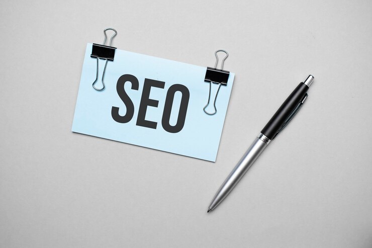 Vista superior de una tarjeta de visita con texto SEO, bolígrafo, clips sobre una superficie coloreada