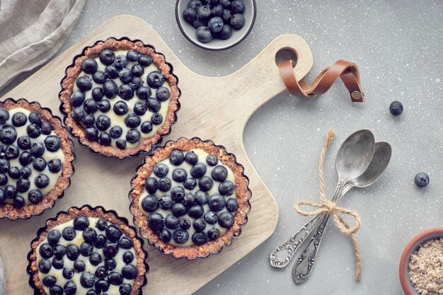 Vista superior de tartas de arándanos integrales con crema de vainilla en tablero de textura ligera