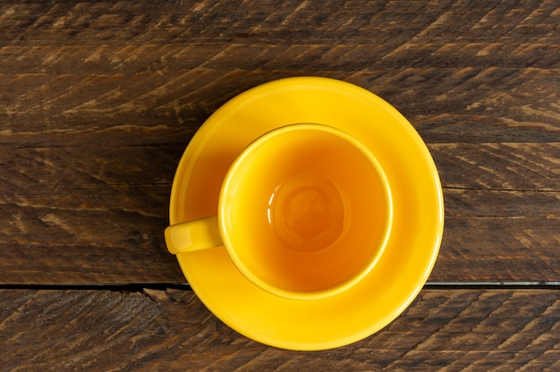 Vista superior de la taza amarilla vacía y el platillo sobre fondo rústico de madera. Vajilla de cocina.