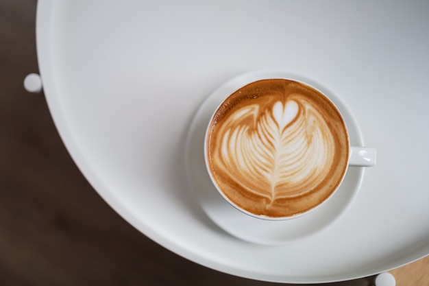 Vista superior de la taza blanca de café con leche caliente con forma de corazón de espuma de leche