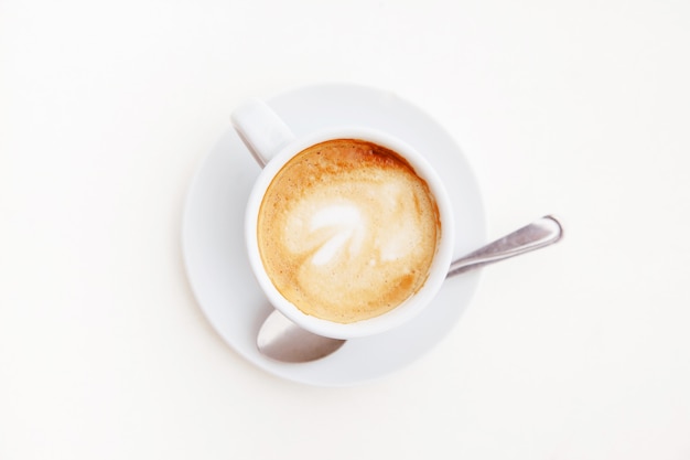 Vista superior de la taza de café aislada en la mesa blanca. Capuchino caliente con espuma en casa.