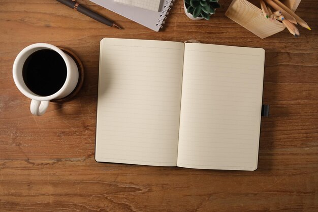 Vista superior de la taza de café del bloc de notas en blanco y la planta en maceta en el escritorio de trabajo de madera