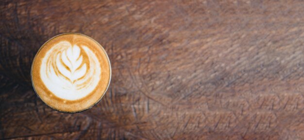 Vista superior de una taza de café caliente con capuchino en bandeja de madera con arte con leche en la mesa de madera