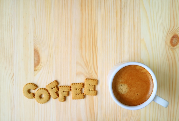 Vista superior de una taza de café caliente en la mesa de madera con la palabra café hecha de galletas