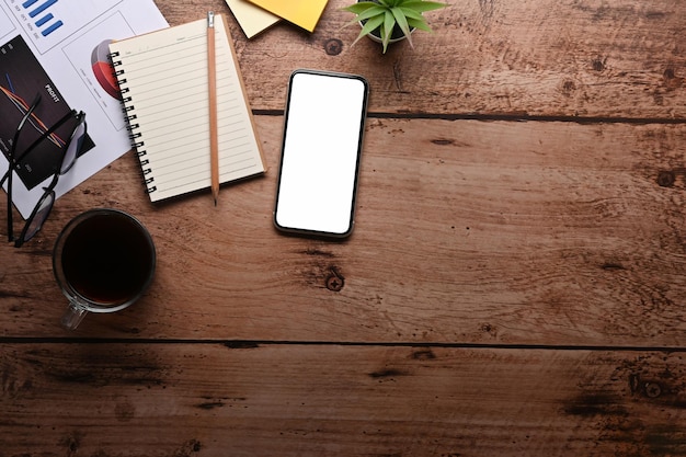 Foto vista superior de la taza de café del cuaderno del teléfono inteligente y los documentos financieros en la mesa de madera
