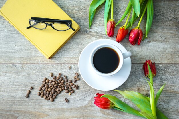 Vista superior de la taza de café y frijoles, ramo de tulipanes rojos, libro