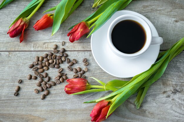 Vista superior de la taza de café y frijoles y ramo de tulipanes rojos