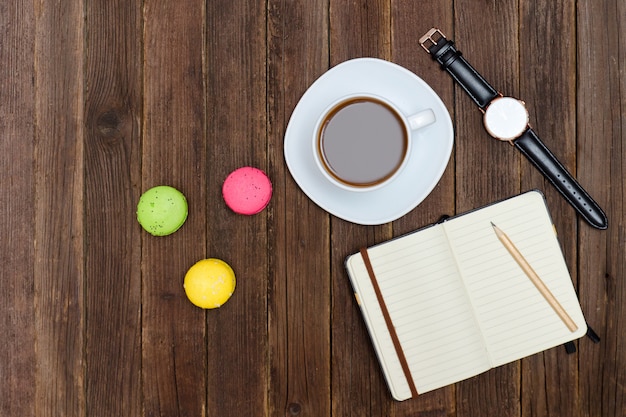 Vista superior de la taza de café, macarons, cuaderno y reloj.