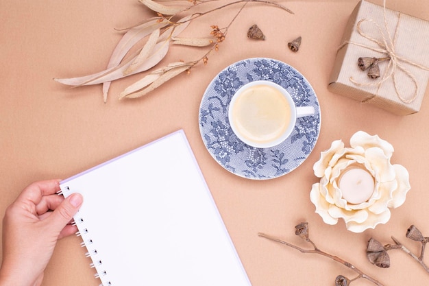 Vista superior de una taza de café y la mano de una mujer sostiene un diario de hojas de eucalipto seco un regalo en p ...