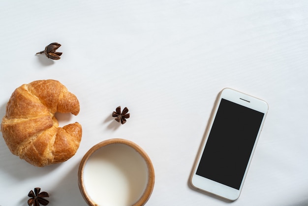 Vista superior de la taza de leche, cuaderno, croissant en mesa de madera