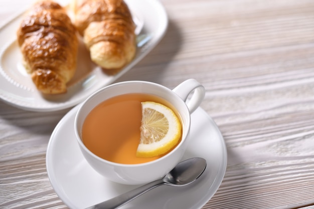 Vista superior de una taza de té con limón y croissant en mesa blanca