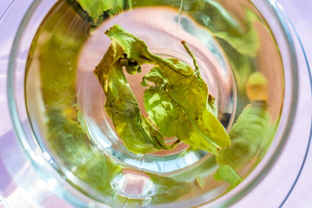 Vista superior de la taza transparente con té verde sobre fondo morado.