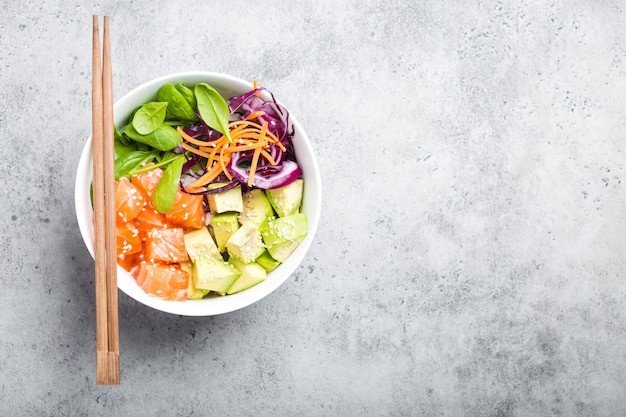 Vista superior del tazón de fuente con salmón crudo fresco y verduras, espacio para texto. Plato tradicional hawaiano sobre fondo de piedra rústica. Concepto de alimentación saludable y limpia. Empuje con rodajas de pescado, espacio de copia