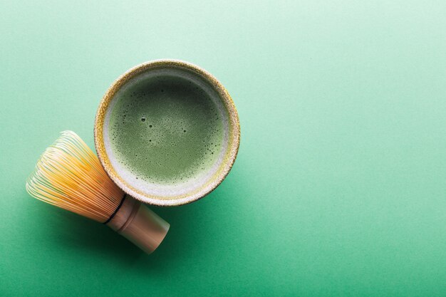 Vista superior de té matcha en un tazón y chasen en superficie verde