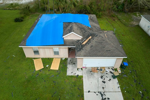 Vista superior del techo de la casa con fugas cubierto con lonas protectoras contra fugas de agua de lluvia hasta el reemplazo de las tejas de asfalto Daño del techo del edificio como secuela del huracán Ian en Florida