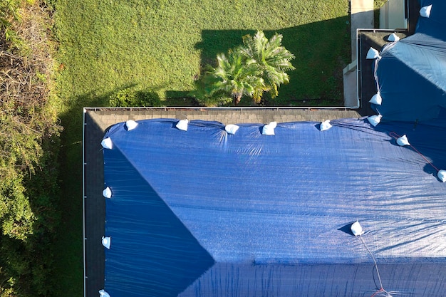 Vista superior del techo de la casa con fugas cubierto con lonas protectoras contra fugas de agua de lluvia hasta el reemplazo de las tejas de asfalto Daño del techo del edificio como secuela del huracán Ian en Florida