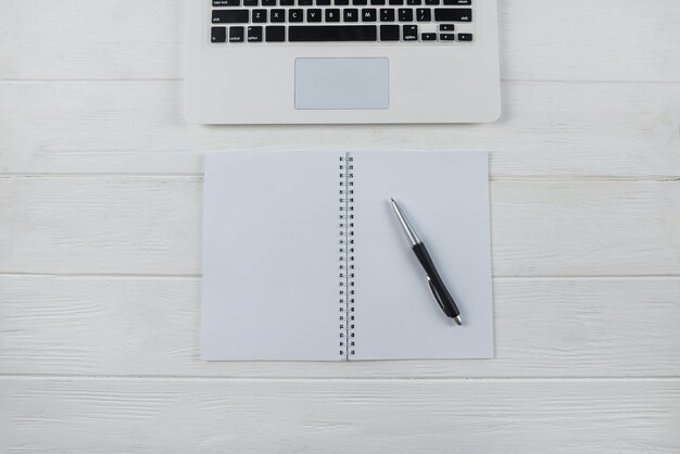 Vista superior del teclado de la computadora portátil con bloc de notas en blanco blanco y bolígrafo en el lugar de espacio de copia de fondo blanco para texto