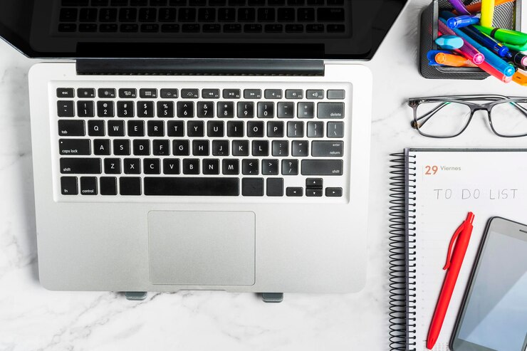 Foto vista superior del teclado de la computadora portátil junto al planificador diario de cosas que hacer anteojos y teléfono celular taza de café