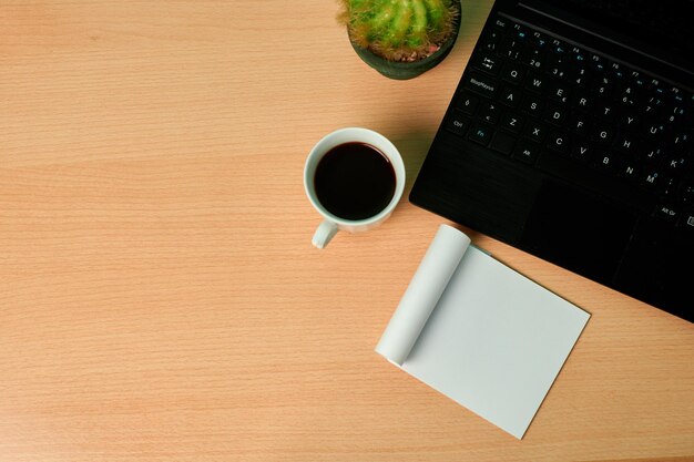 Vista superior de un teclado, planta, taza de café y papel en blanco sobre un escritorio de madera. copia espacio