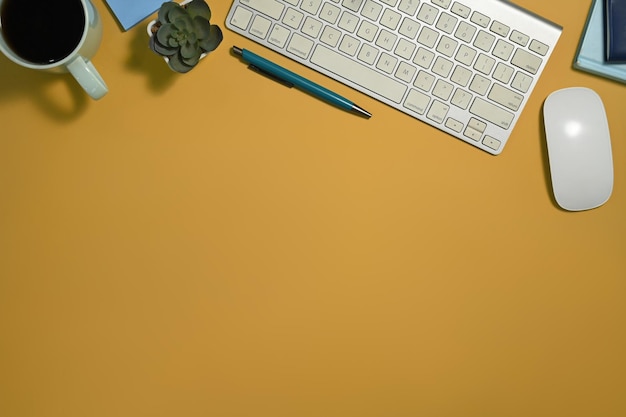 Vista superior del teclado vasos de taza de café y cuadernos sobre fondo amarillo con espacio