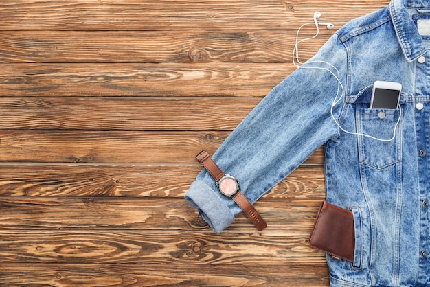 Foto vista superior del teléfono inteligente de la chaqueta de mezclilla y accesorios sobre fondo de madera