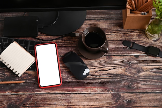 Vista superior de teléfono inteligente con pantalla blanca, portátil, reloj inteligente y taza de café en la mesa de madera.