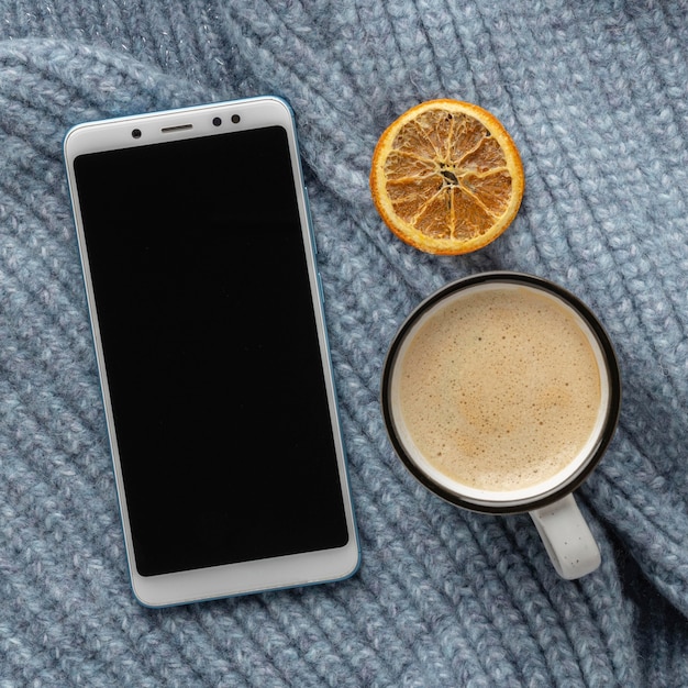 Foto vista superior del teléfono inteligente en suéter con taza de café y cítricos secos