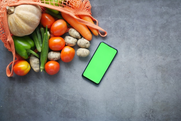 Vista superior del teléfono inteligente con verduras frescas en la mesa.